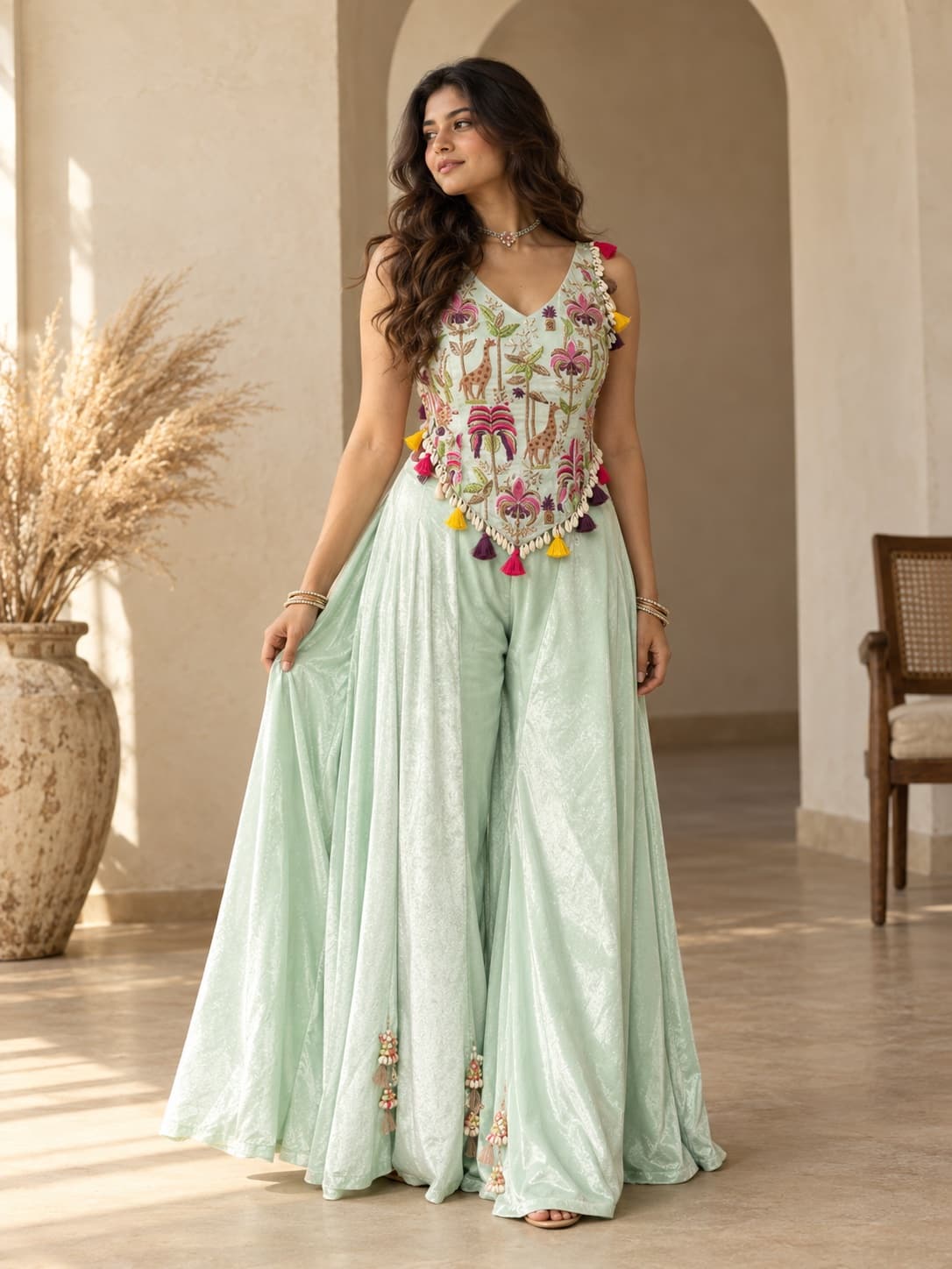 A woman in a mint sharara set with a giraffe and palm embroidered corset top trimmed with cowrie shells and tassels