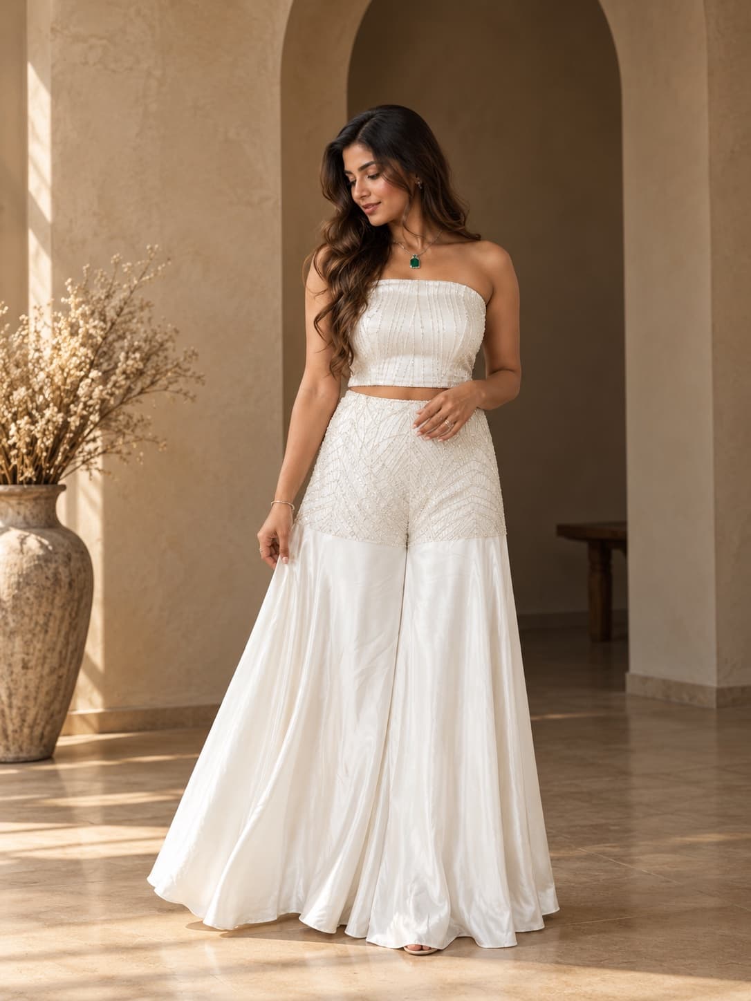 A woman in a white beaded strapless corset top and a satin sharara with a sequinned hip yoke